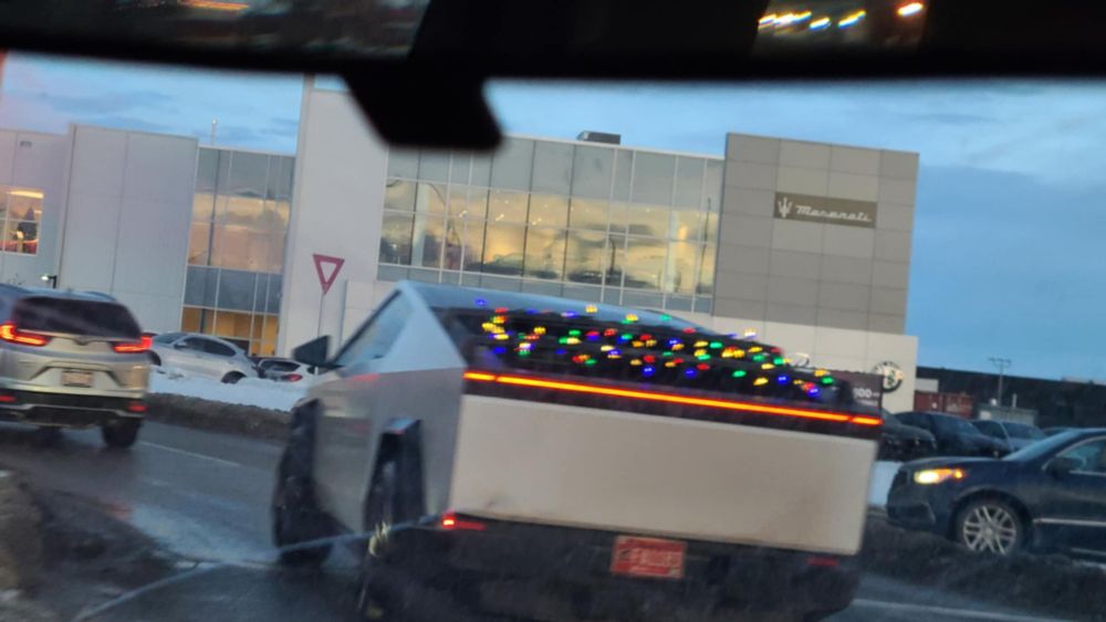 A tesla cybertruck with Christmas lights in the back window driving on a road