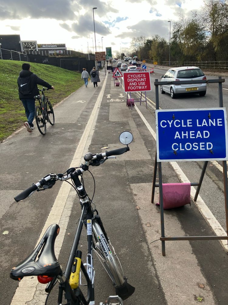 Picture shows cycle lane closed and cyclists dismount and walk signs on uphill section of shared use pavement. 