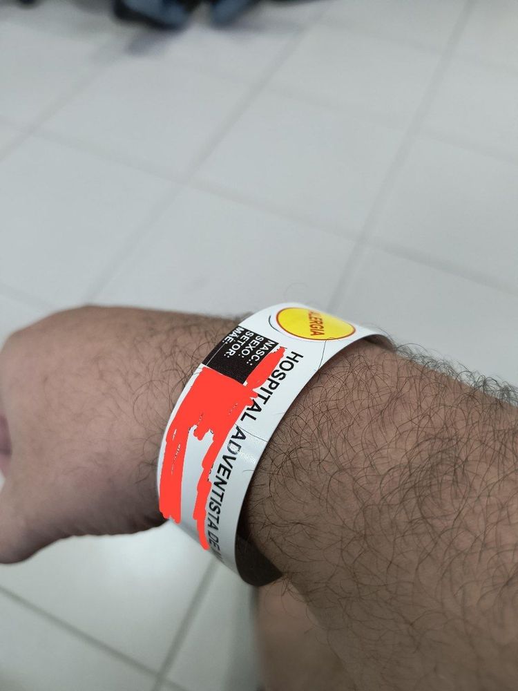 Foto de uma pulseira hospitalar. As informações pessoais foram cobertas por uma marcação em vermelho e é visível apenas a frase "Hospital Adventista" 