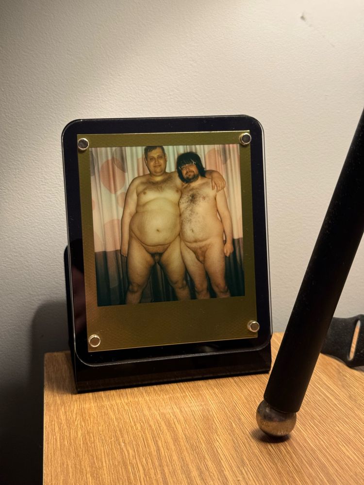 A framed Polaroid photo on a bedside table, showing me and a friend naked
