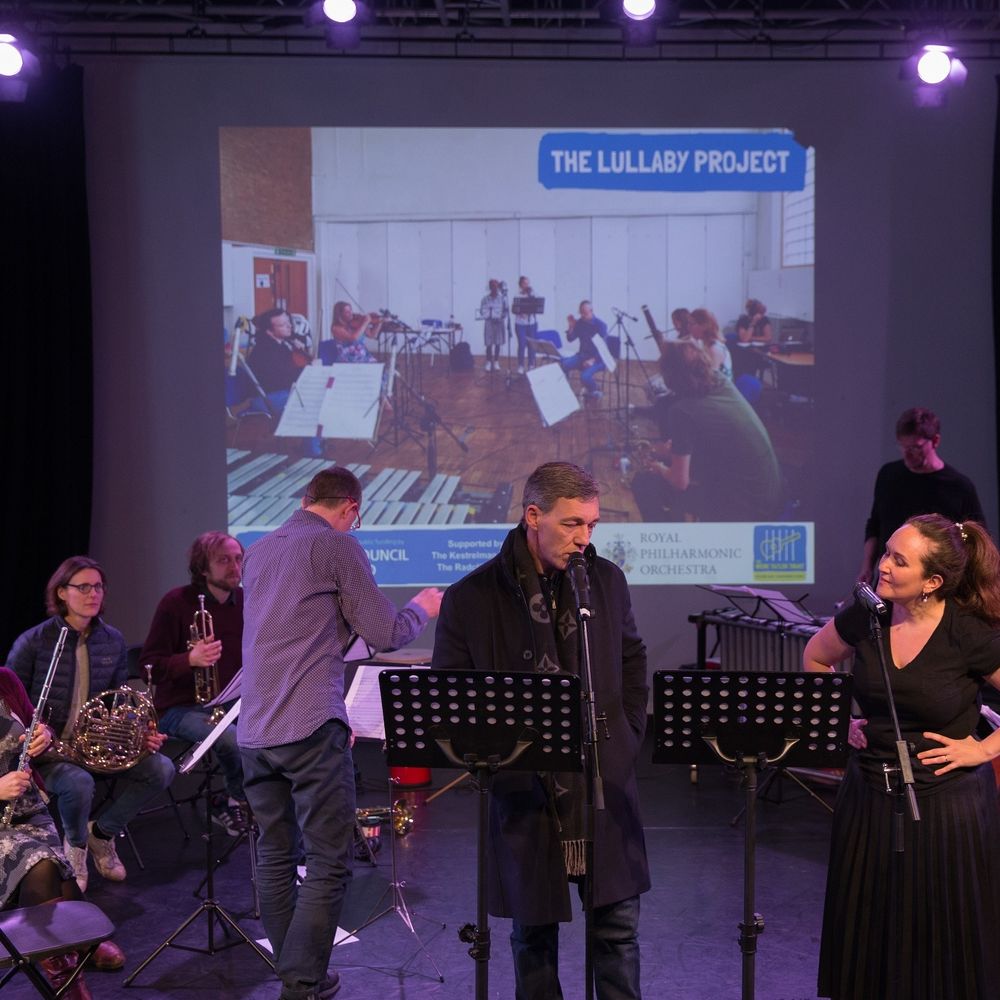 A man in a coat sings into a microphone on stage with classical musicians 