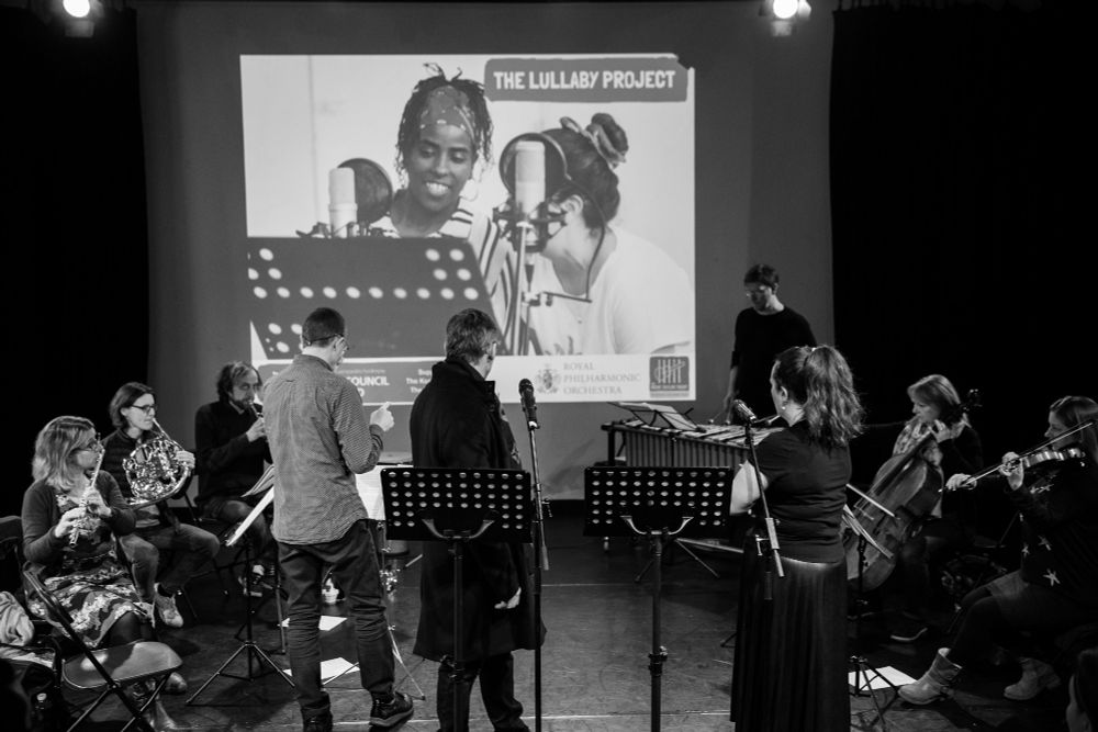 A group of performers facing away from the camera, including classical musicians 