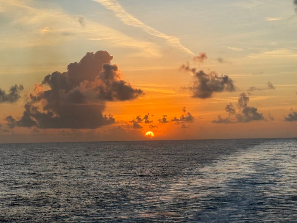 The sun has just crested the horizon of the open ocean. With orange and yellow reflecting off the clouds above.