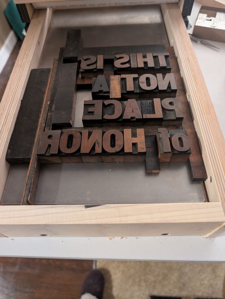 Wood type on the bed of a Provisional Press held in place with various furniture reading "THIS IS NOT A PLACE of HONOR" because I only have so many of uppercase O.