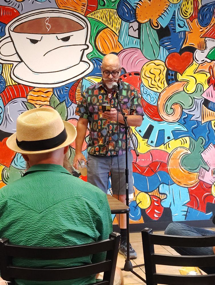 A man in a colorful shirt in front of a bright mural.