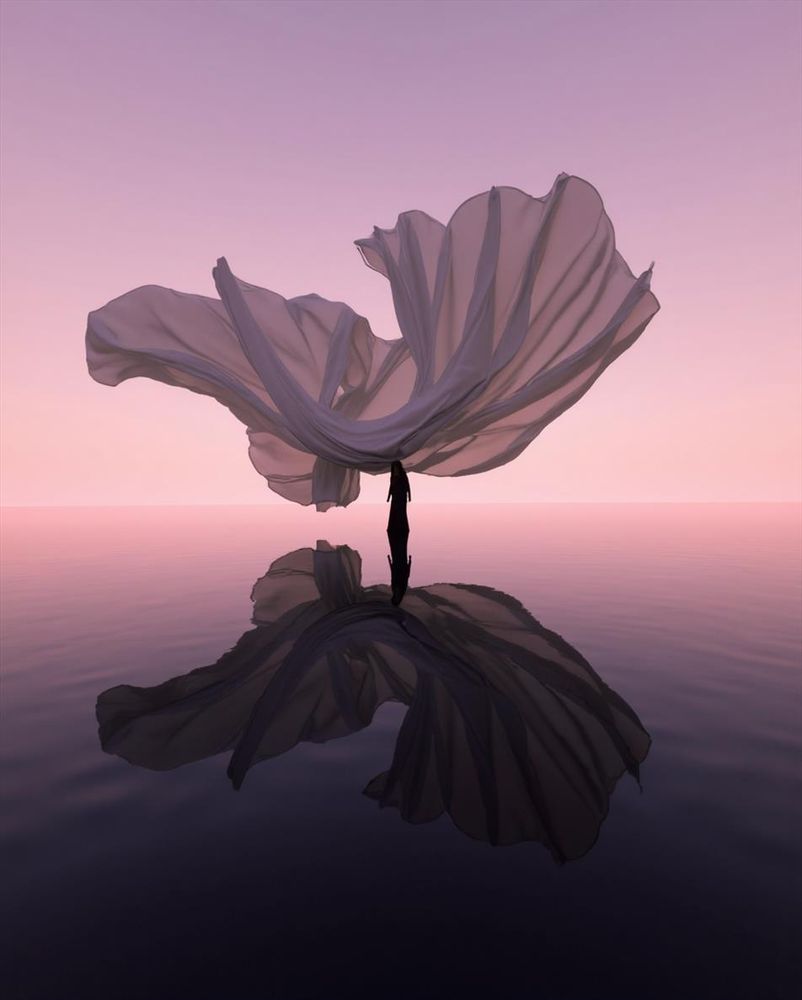 A silhouetted figure stands on still water at twilight, holding a large, semi-translucent fabric that billows overhead in a petal-like shape. The pastel-pink sky softly meets the water at the horizon, creating a serene, dreamlike scene.