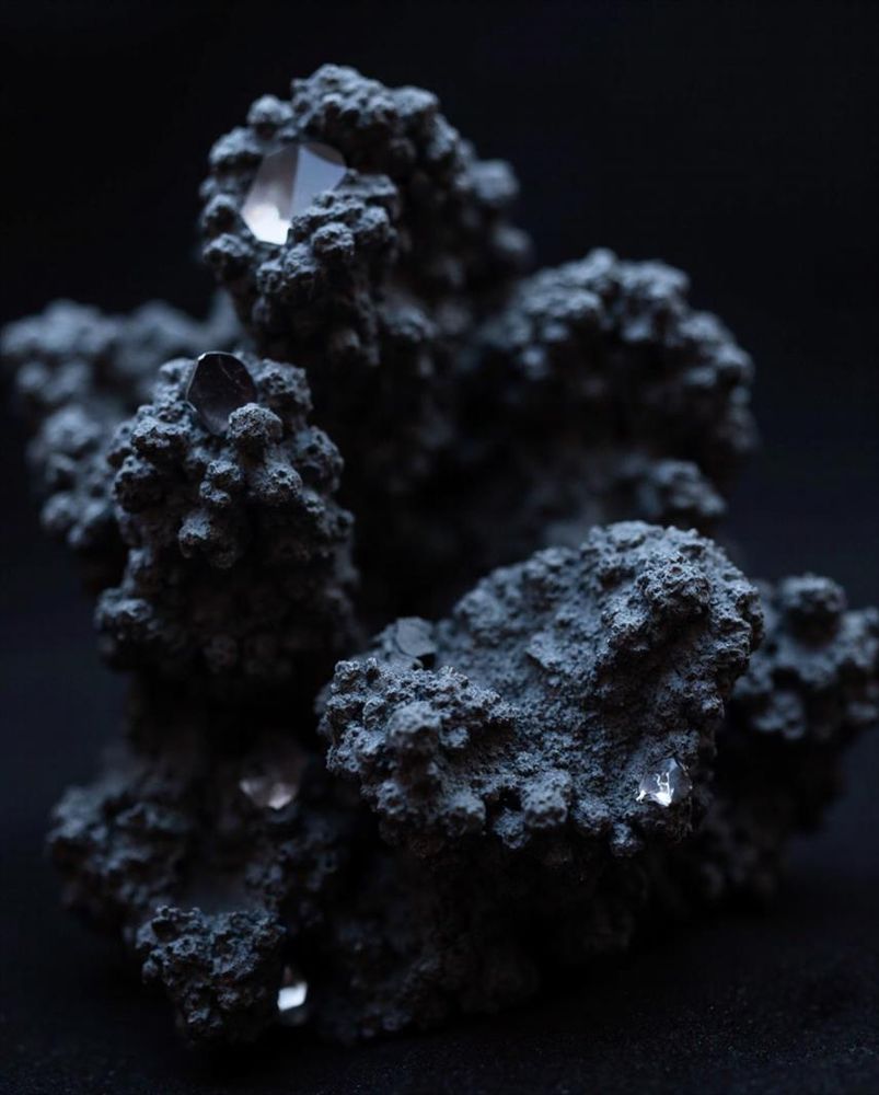 A close-up of a rugged, dark mineral formation cradling embedded reflective crystals. The interplay of rough textures and glistening facets evokes a sense of mystery and contrast.