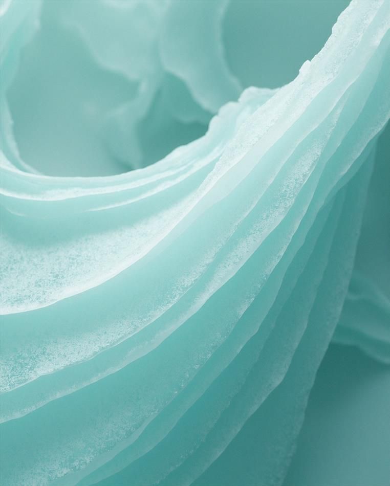 A close-up of delicate, layered formations in soft turquoise, resembling frozen waves or eroded mineral surfaces. The image conveys a sense of fluidity captured in stillness.