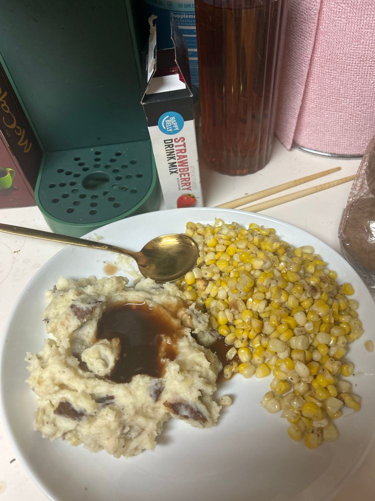 a plate of mash potatoes with skins and brown gravy next to a large amount of sweet corn. 
