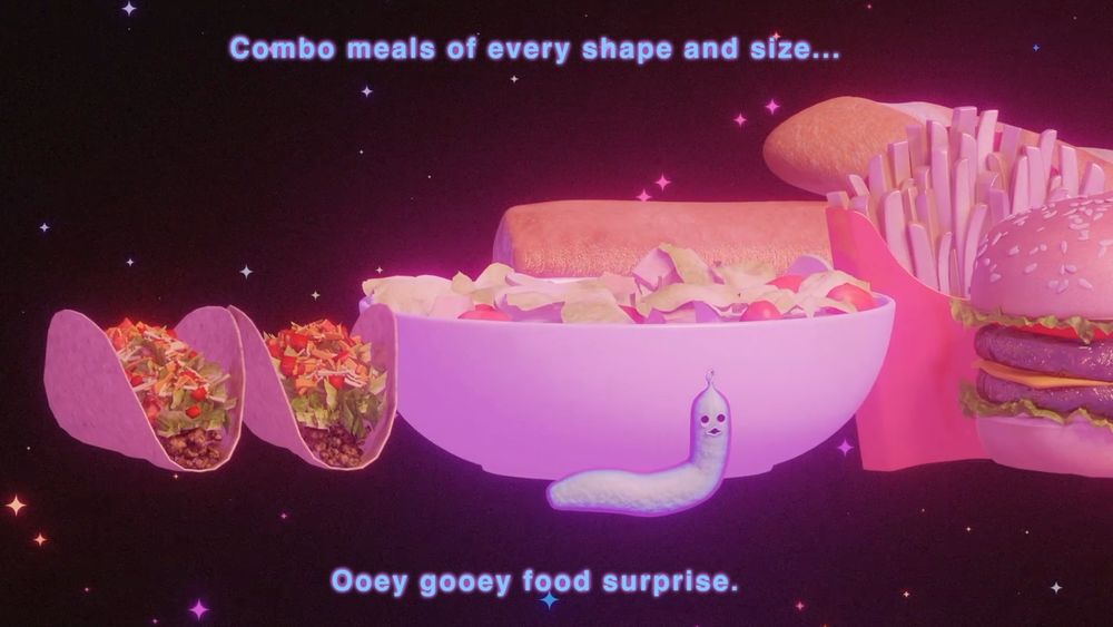 A screencap from the film "Boys Go To Jupiter." It shows an alien worm in front of a bunch of snacks saying "Combo meals of every shape and size... ooey gooey food surprise"
