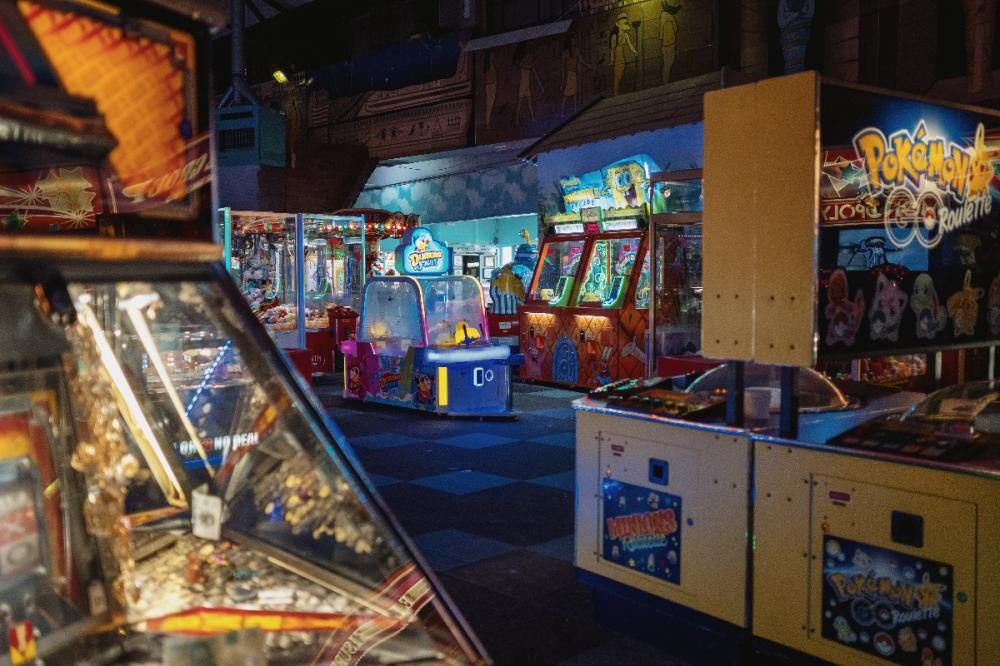 Arcade games including claw machines lit from within, sit in a dark, empty arcade.
