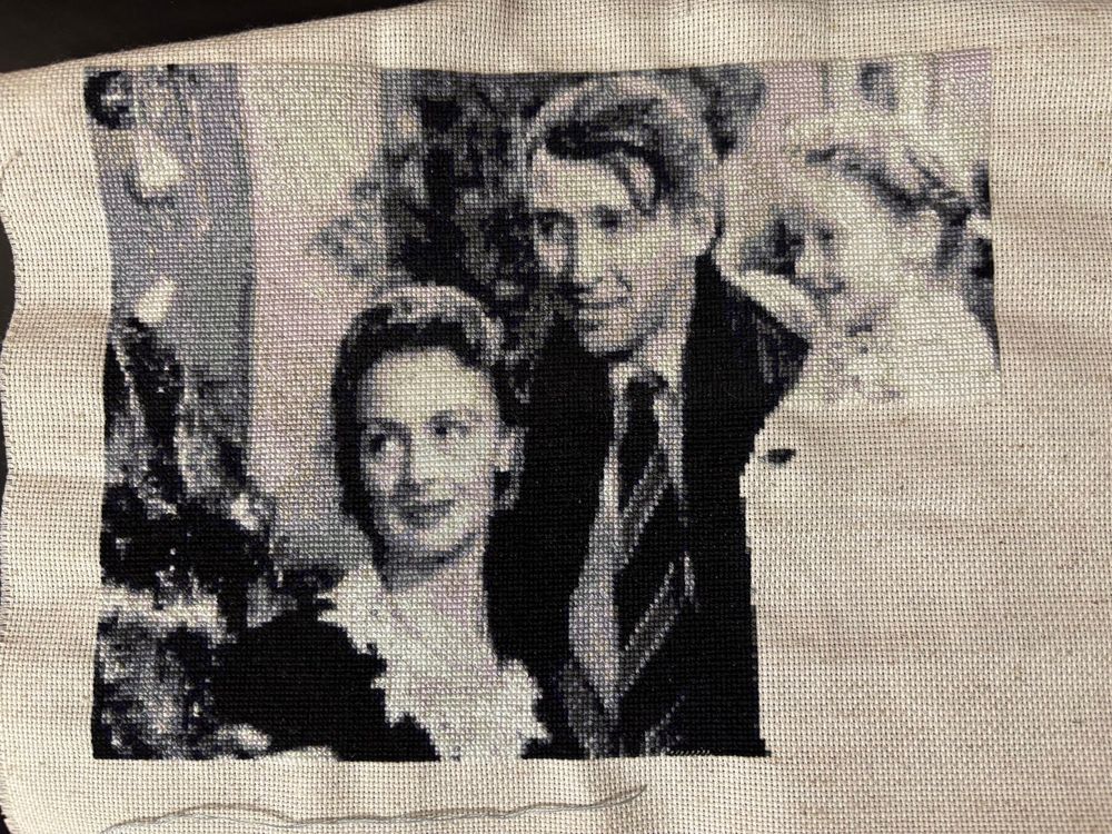 Monochrome cross stitch of the final scene of It’s A Wonderful Life. The faces of Jimmy Stewart, Donna Reed, and Karolyn Grimes are visible.