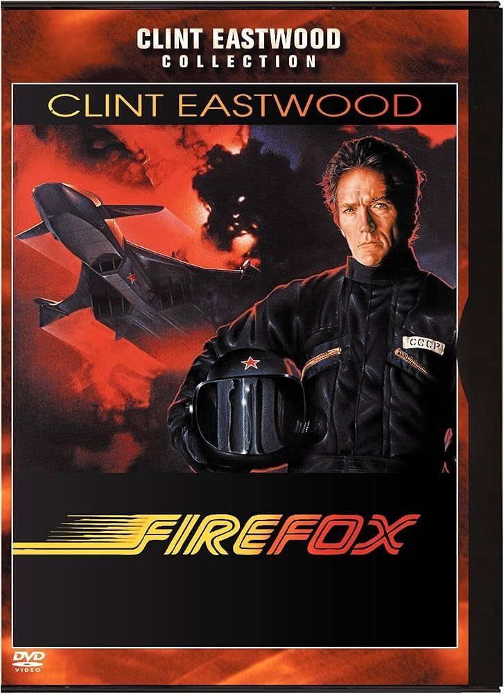 A man in a black suit holding a black helmet. There is a plane in the background 
