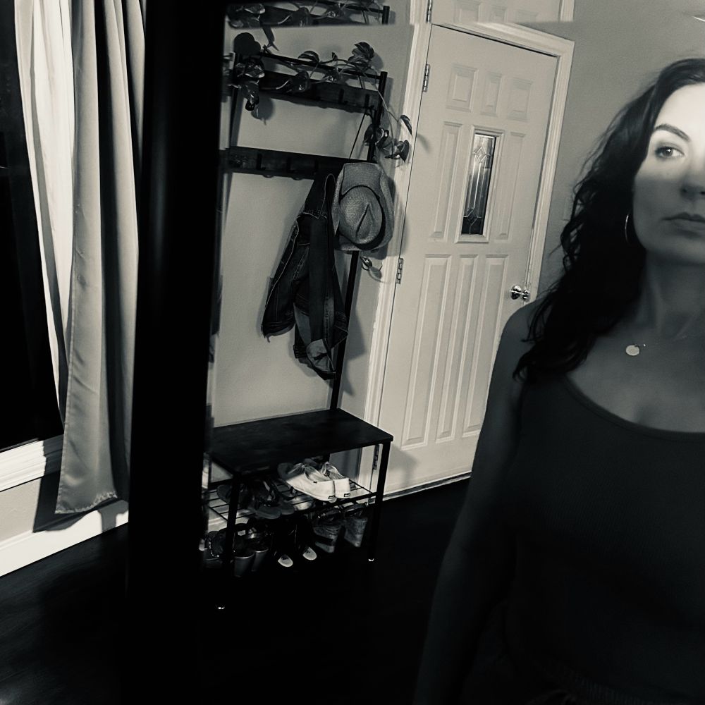 Black-and-white self portrait of Lyla in standing in front of a mirror in their living room.      Only half their face is in the frame, and they are lit from forehead to just above the tip of their nose. The mirror blocks the rest of the light, an accidental cucoloris. 

When they are watching themselves dance, it looks very neat, but it’s tricky to show that.