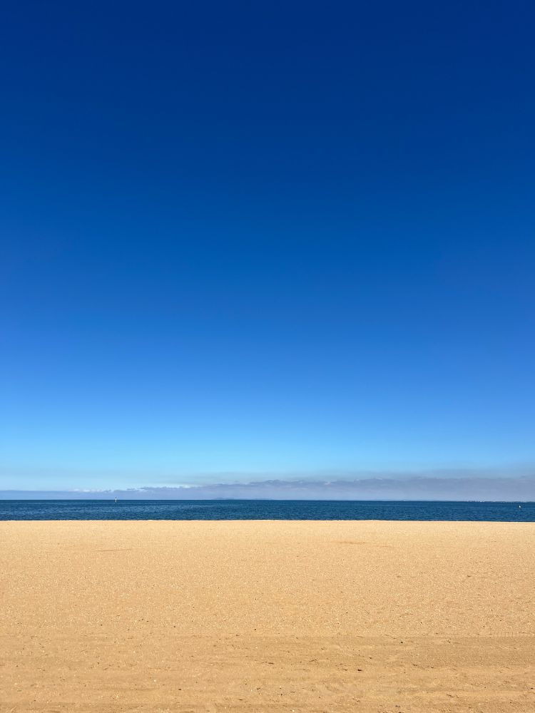 A photo of Brighton Beach in Melbourne, Australia, depicting golden sands, the sea, and clear blue skies.