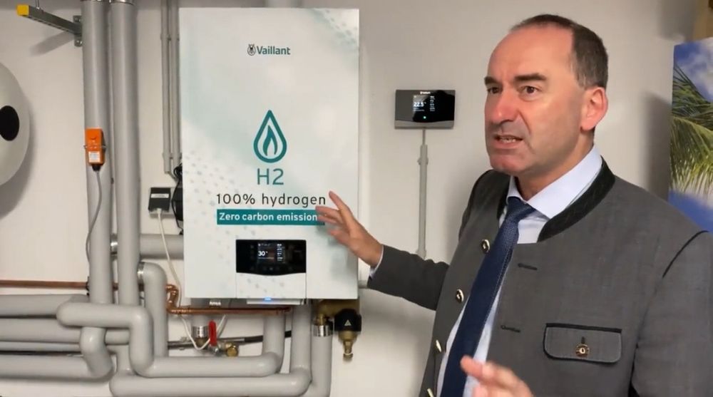 Hubert Aiwanger steht sprechend vor einer Vaillant-Therme mit der Aufschrift “100% Hydrogen”.