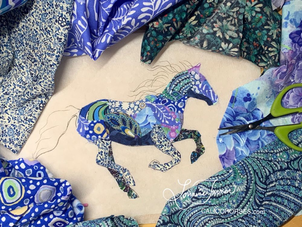 A fabric collage of a galloping horse created with scraps of blue, navy, lavender and purple cotton fabrics.