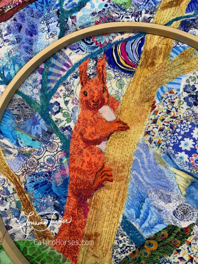 A textile illustration of a red squirrel on a brown tree against a blue background 