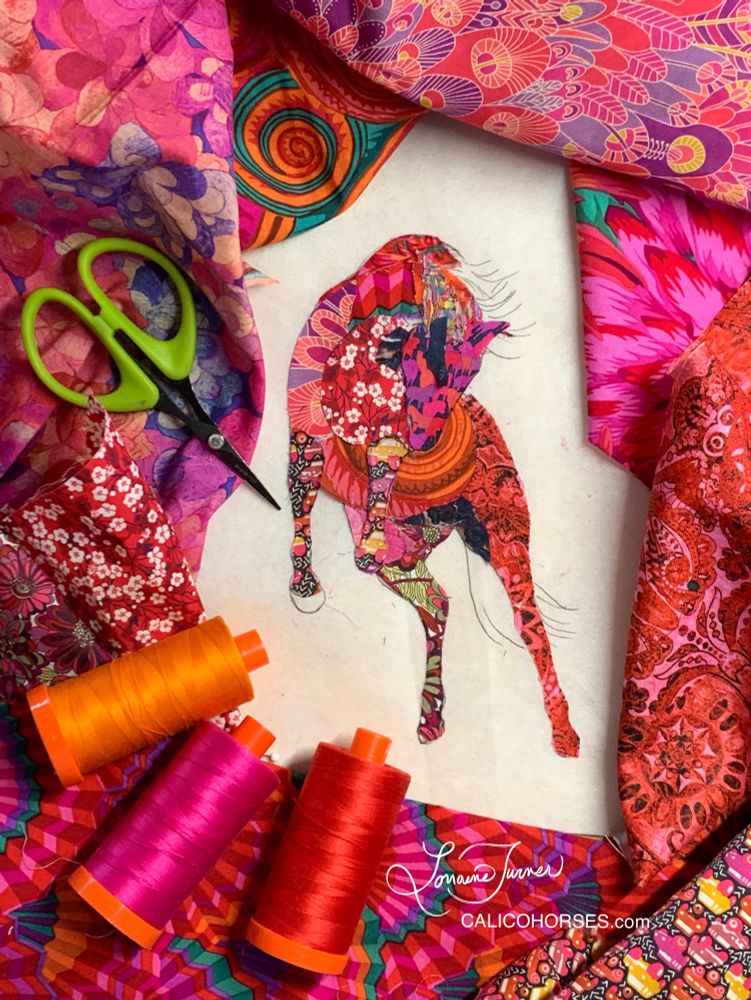 A red, magenta, maroon and navy wild horse created with scraps of fabric. Matching fabrics and threads surround the work in progress 