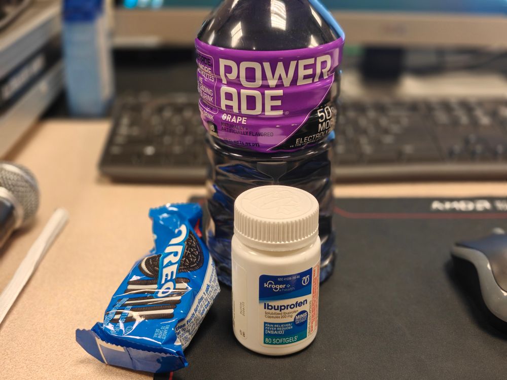 A bottle of Grape Powerade, a bottle of ibuprofen, and some Oreo cookies.