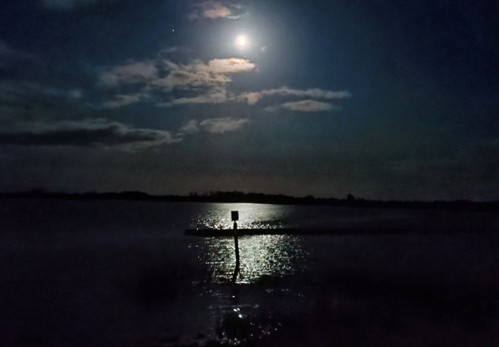 The full moon shines in a cloudy sky on a direction guide positioned in the dark waters of the River Shannon, Ireland.