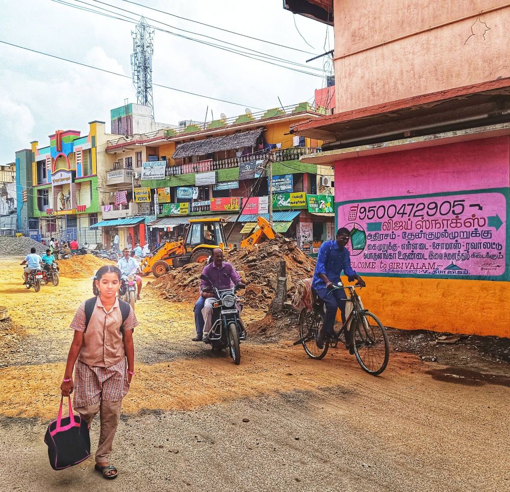 A young Indian girl, eyes downcast, wearing a school uniform and carrying a rucksack on her back and a tote bag in her right hand walks alone along a road under construction, an earthmover and gravel and clay piles clearly visible behind her. 

Around her are men weaving through the rubble on cycles. There is a row of three storey buildings in the background. A sign in mostly Tamil script is hand-painted on a nearby wall, with a cellphone number and 'Welcome To Girivalam' text in English. 

The lyrics are from a traditional spiritual which dates back to the era of slavery in the United States, and the original score of "Motherless Child" was  by William E. Barton, D.D., 1899. An early performance of the song was in the 1870s by the Fisk Jubilee Singers, and Van Morrison recorded a version for his 1987 album 'Poetic Champions Compose'. 

Tiruvannamalai, Tamil Nadu, India.