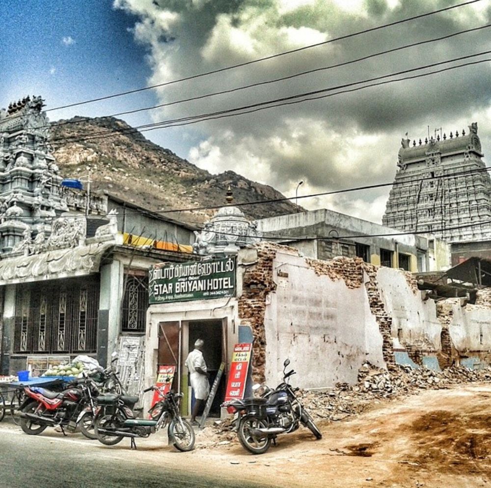 Motorcycles parked outside 'Star Biriyani' restaurant, with Mount Arunachala and Arunachaleswarar Temple in the background. A next-door building site has been cleared to facilitate construction of an apartment block.