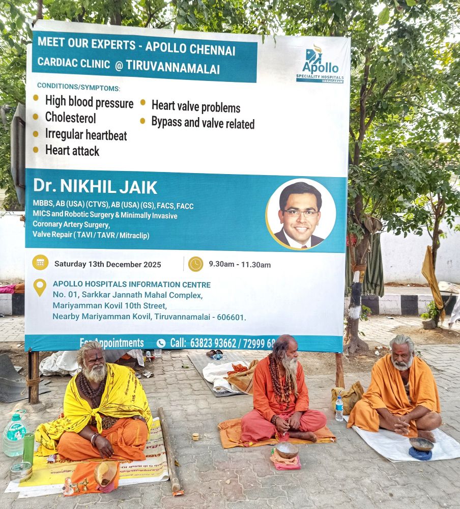 'MEET OUR EXPERTS!'

At the foot of a large promotional banner sit three sadhus, Hindu religious ascetics, who have renounced worldly life to pursue spiritual discipline (sadhana) and to rely on charity for sustenance. 

All three have grey beards and two of them wear rudraksha beads around their necks. Each sits cross-legged on their own covering on the ground with a small container before them to collect alms from pilgrims passing along the girivalam route.

The text on the promotional banner behind them reads:

MEET OUR EXPERTS - APOLLO CHENNAI - CARDIAC CLINIC @ TIRUVANNAMALAI - SPECIALITY HOSPITALS, VANAGARAN

CONDITIONS/SYMPTOMS:

High blood pressure
Cholesterol
Heart valve problems
Irregular heartbeat
Bypass and valve related
Heart attack

Dr. NIKHIL JAIK, MBBS, AB (USA) (CTVS), AB (USA) (GS), FACS, FACC MICS and Robotic Surgery & Minimally Invasive Coronary Artery Surgery, Valve Repair (TAVI/TAVR/Mitraclip)

9.30am -11.30am
Saturday 13th December 2025

APOLLO HOSPITALS INFORMATION CENTRE No. 01, Sarkkar Jannath Mahal Complex, Mariyamman Kovil 10th Street, Nearby Mariyamman Kovil, Tiruvannamalai - 606601.

For appointments
Call: 63823 93662 / 7299968