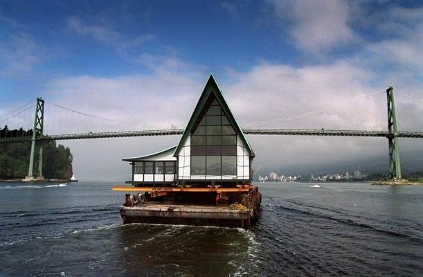 An A-Frame house on a barge is sailing toward the Lions Gate Bridge on its way to Vancouver Island