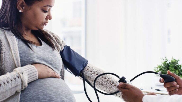 Woman visibly pregnant with a blood pressure cuff on her arm