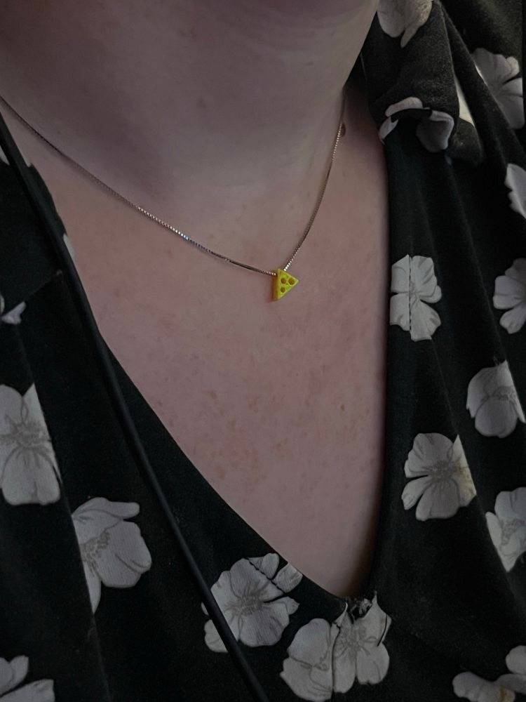 close up of lexi’s neckline, showing necklace details to be a tiny yellow opal piece shaped like a cheese wedge, dangling from a silver chain and sitting above her adorable freckled cleavage. 