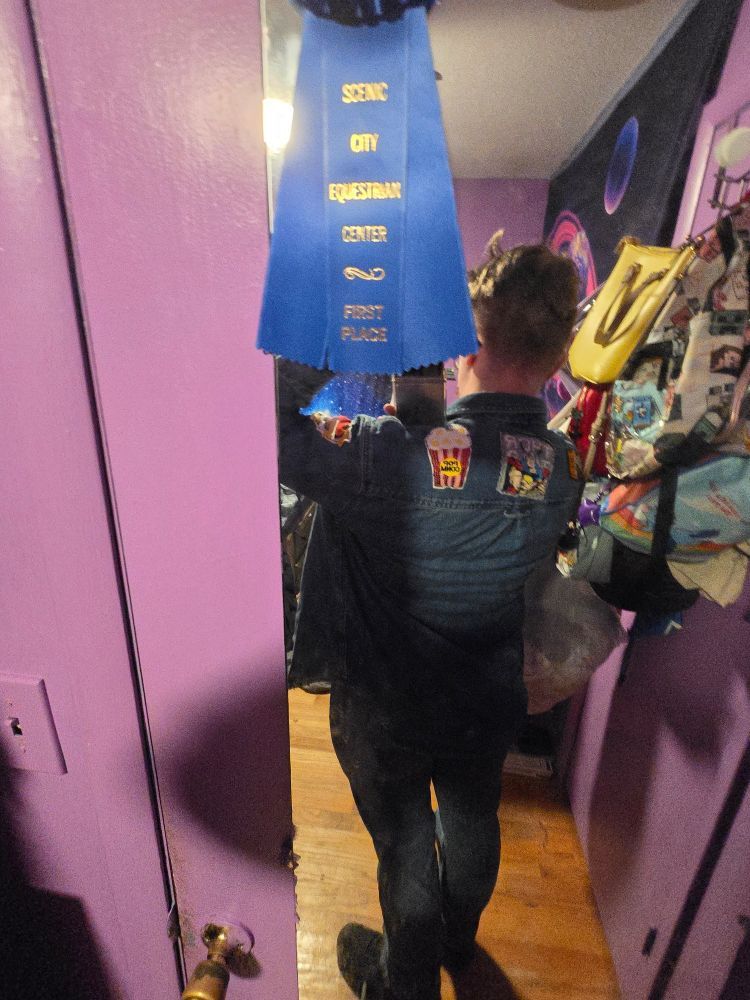 A mirror selfie showing the back of a. Oversized denim short with patches on it