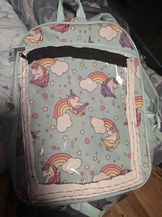 A unicorn backpack with a transparent pocket sewn onto the front of it