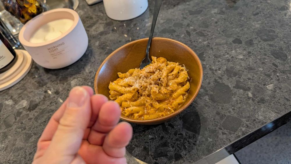 A bowl of chicken pasta in creamy tomato sauce topped with shredded patmesean and cracked black pepper, sitting on a black stone countertop next to a candle.
