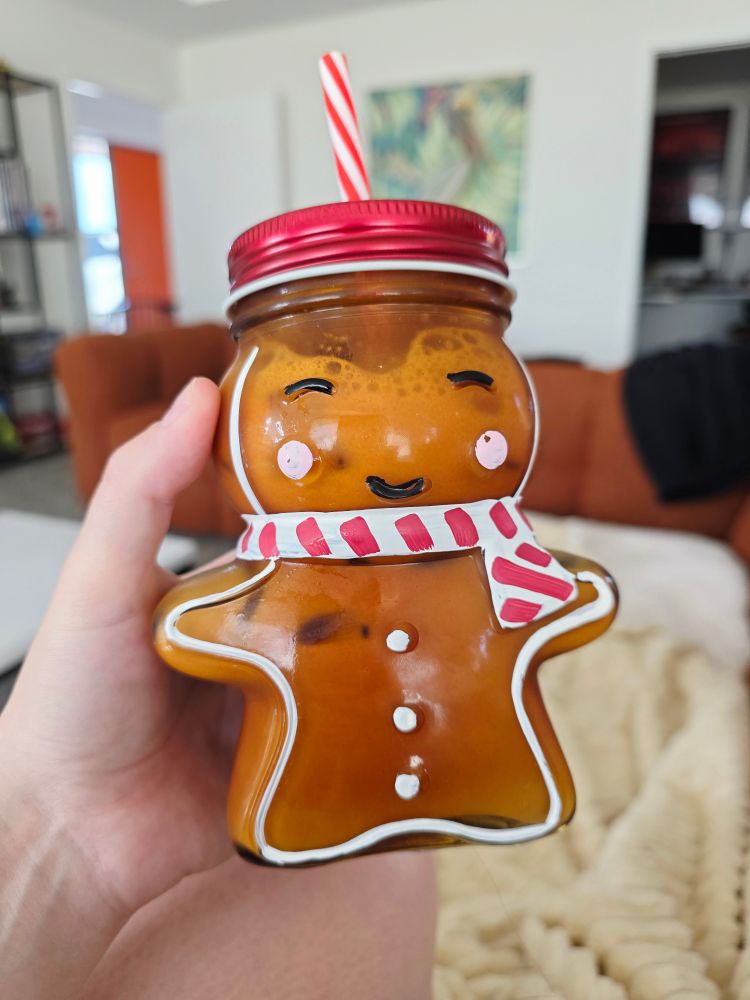 An iced brown sugar double espresso coffee with whole milk in a glass cup that is shaped like a smiling ginger bread man. 