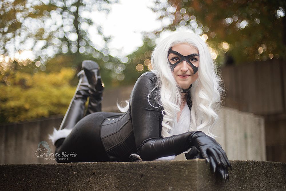 Cosplayer dressed as black cat from marvel, lounging stomach down on a cement block 