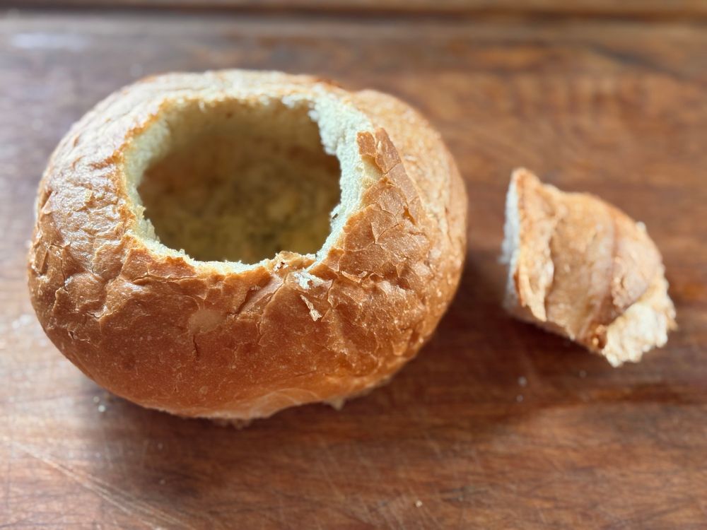 Empty baked bread bowl with top removed and set aside. 