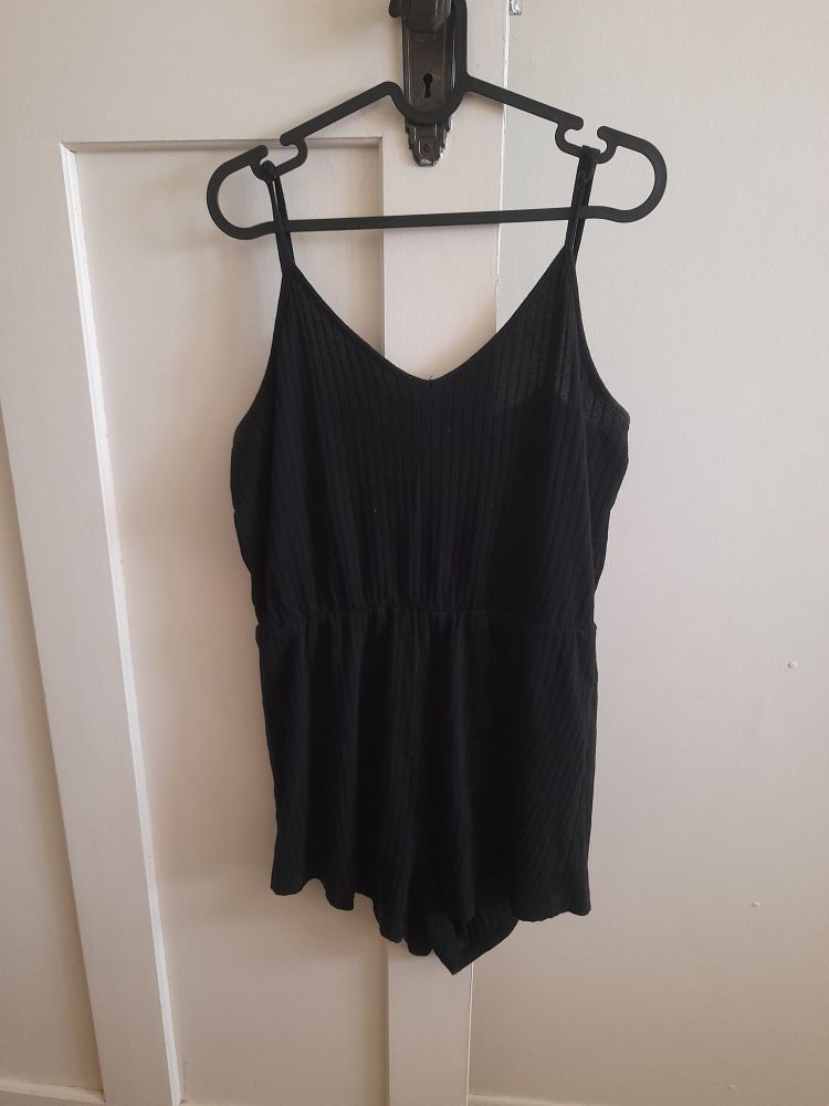 The black jumpsuit hanging from a coathanger on a doorknob of a white door. 