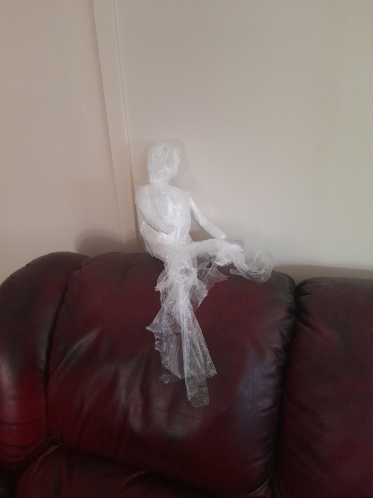 A little ghost man made of plastic bags lounging on the back of a couch.