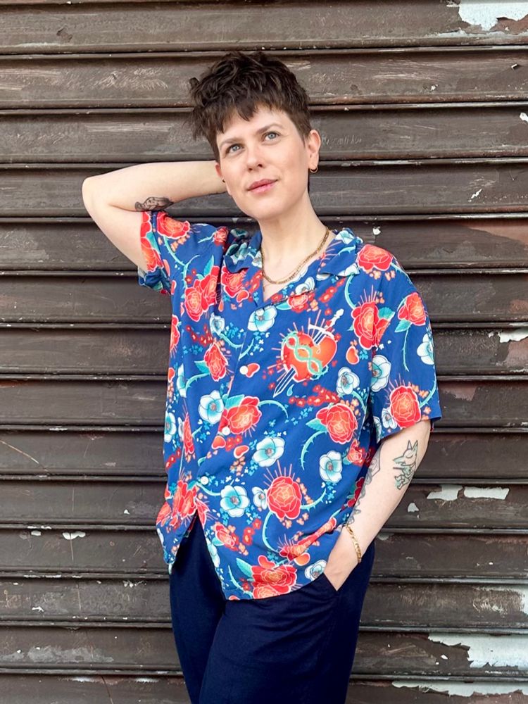 I’m wearing the blue floral Romeo button up from Romeo+Juliet, blue slacks, and black boots. I’m standing in front of a closed shop security gate, a hand in my pocket and a hand fiddling with my hair. I’m smiling a little. I have sleepy eyes.