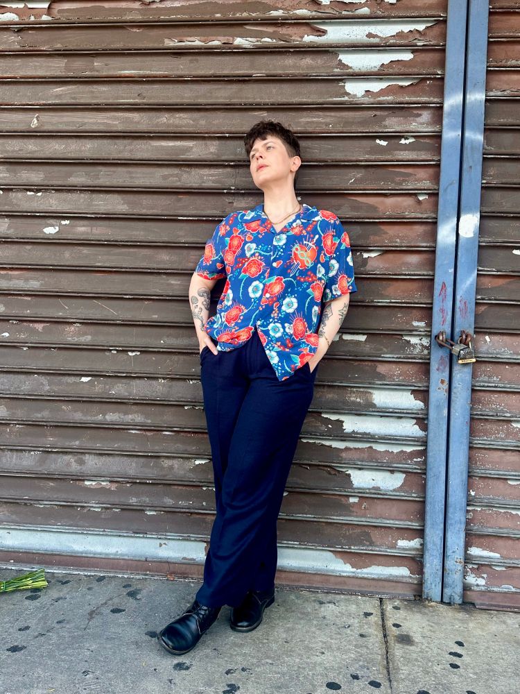I’m wearing the blue floral Romeo button up from Romeo+Juliet, blue slacks, and black boots. I lean against a closed and locked shop security door, looking up.