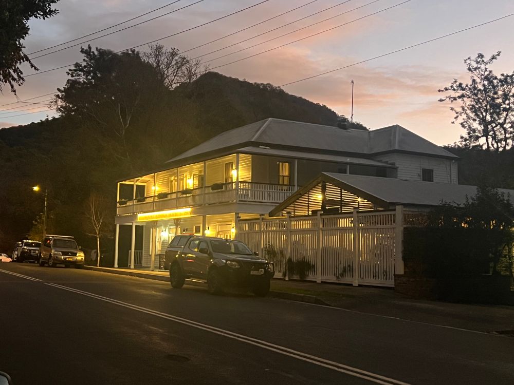 White weatherboard pub with a verandah and balcony, with a silhouette of a mountain in the background.
