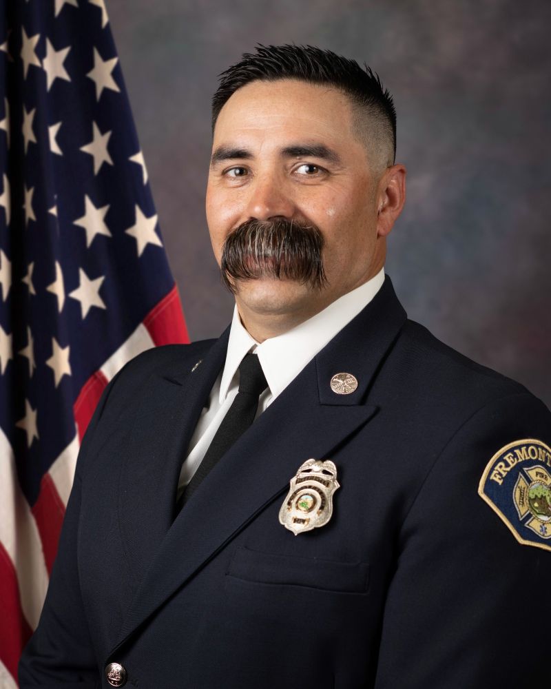 a (now deceased, rip) firefighter in his professional photo, wearing dress blues for a suit & fresh high and tight haircut; his mustache is like 4 inches long and combed straight down which covers his mouth