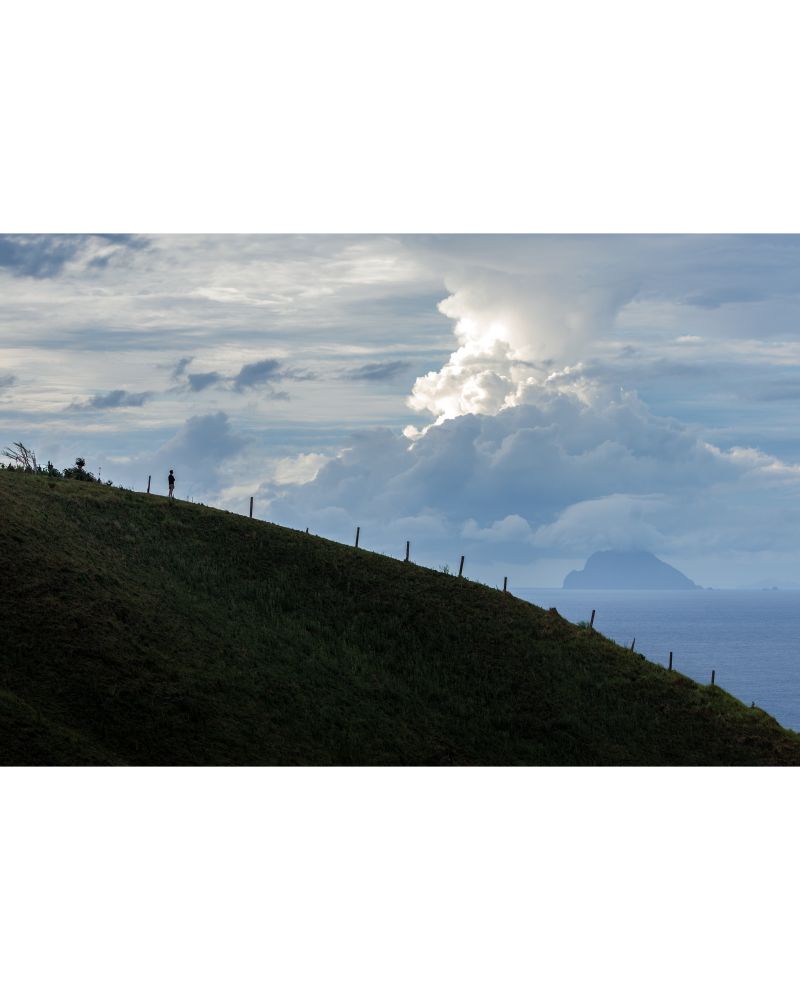 A person on a hill looking at a cloud formation.
