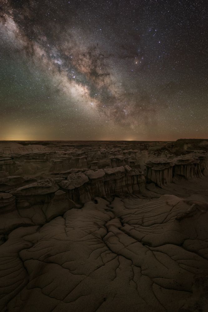 The Milky Way above a layered landscape of hoodoos and cracked ground. 