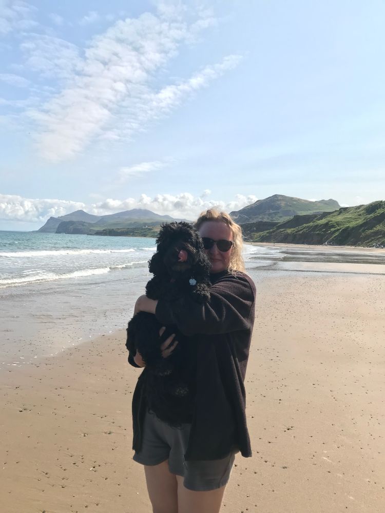 Helen holding a small black dog on a beach