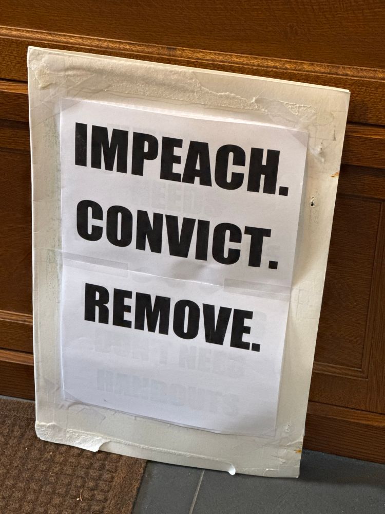 A sign that reads “impeach. Convict. Remove.”