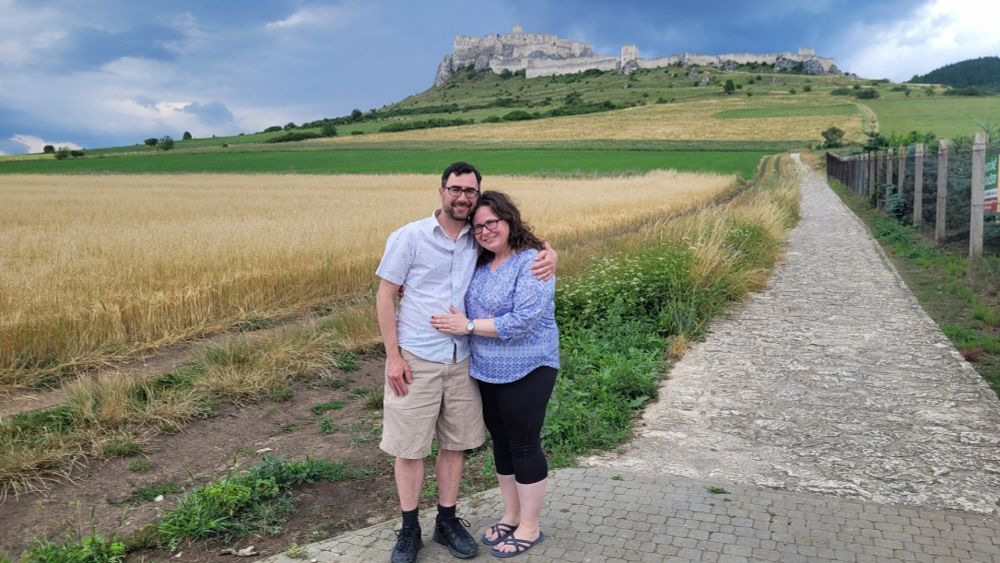 A couple poses under the ruins of Spiš Castle in Eastern Slovakia with some threatening clouds overhead.