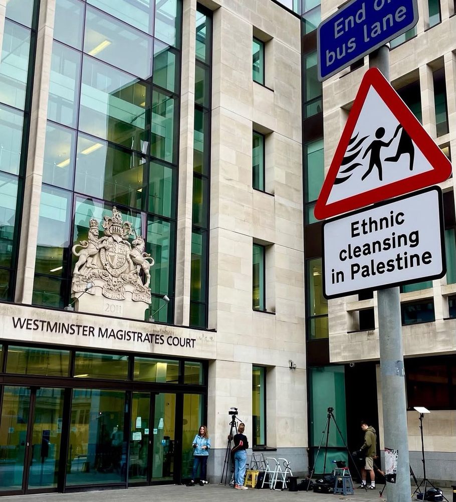 A modified "Warning: Children Crossing" street sign outside Westminster Magistrates Court. It shows children fleeing war and has the text "Ethnic cleansing in Palestine"