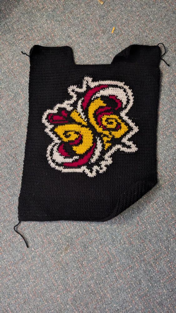 A black crocheted panel with the S logo from Sk8 the Infinity in the center
